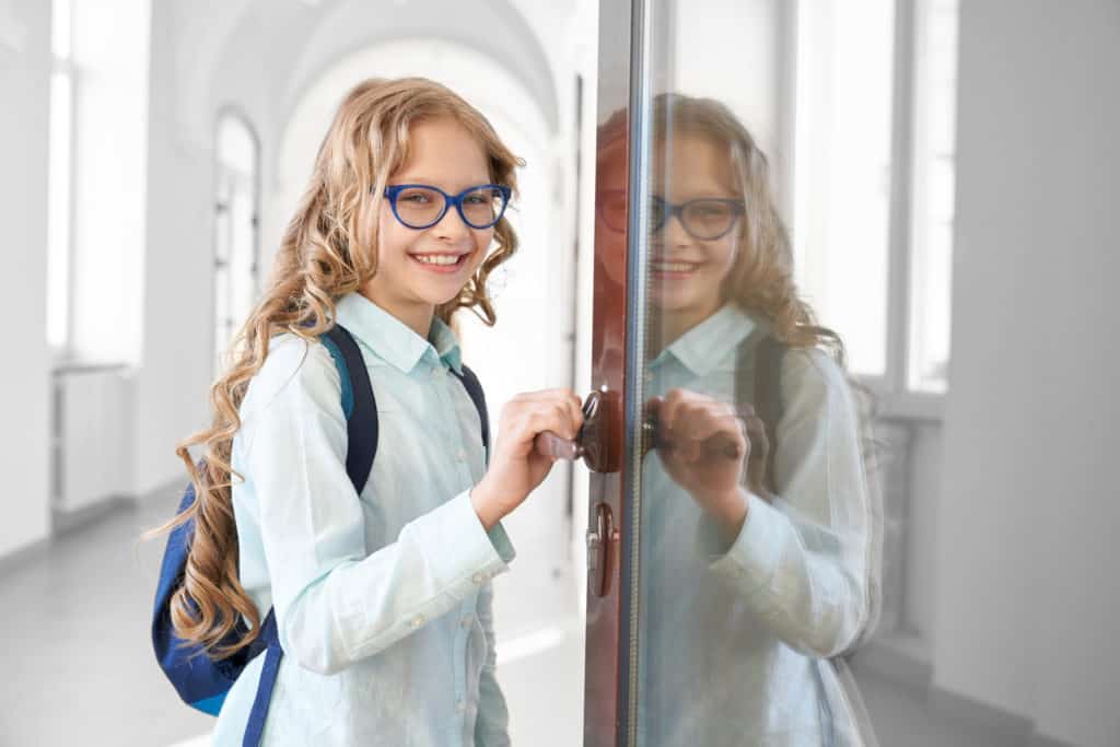 Happy Blonde School Girl Holding Opened Door.